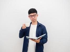 Asian man wearing glasses reading the book in hand and drinking coffee cup on white background photo