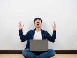 Asian man with laptop cheerful and feeling happy looking up at space sitting on the floor photo