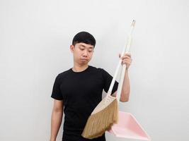 Asian man holding dustpan and broom feeling bored to clean house on white background photo