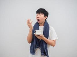 Asian man feeling sleepy and yawn holding coffee cup with towel before wake up at the morning on isolated white photo