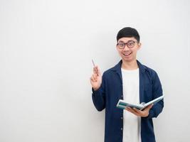 Asian young man wearing glasses cheerful get idea smile face point pen up and holding the book in hand photo