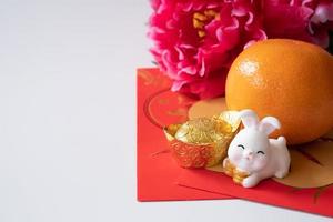 año nuevo chino del concepto del festival del conejo. naranja, sobres rojos, dos conejos y lingotes de oro decorados con flores de ciruela sobre fondo blanco. foto