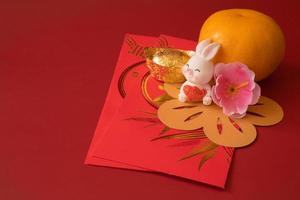Chinese New Year of the rabbit festival concept. Mandarin orange, red envelopes, rabbit and gold ingot decorated with plum blossom on red background. photo