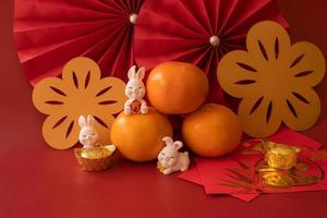 Chinese New Year of the rabbit festival concept. Mandarin orange, red envelopes, rabbit and gold ingot with red paper fans. Traditional holiday lunar New Year. Chinese character cai meaning money. photo