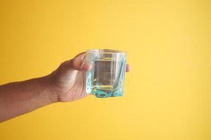 sosteniendo un vaso de agua contra el fondo amarillo foto