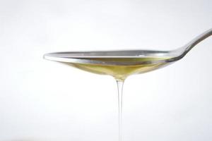 olive oil drop from a silver spoon against white background photo