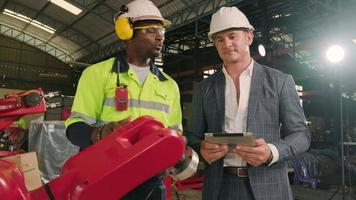 An African American engineer demonstrates smart robotic arm control to customer in mechanical manufacturing factory, intelligent automatic machines in industrial business, and futuristic technology. video