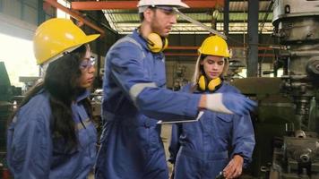 een industrieel arbeiders team in beschermend en veiligheid uniformen en harde hoeden, mannetje manager, en zijn collega's wandelen en bespreken metaalwerk in fabricage fabriek. professioneel productie ingenieur. video