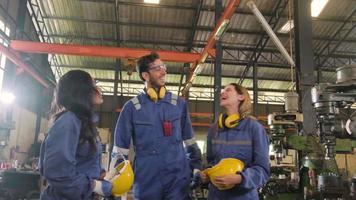 A professional industrial worker's team is resting after work. Male manager and female colleagues taking off helmets and relaxing at metalwork machines in manufacturing factory, production engineer. video