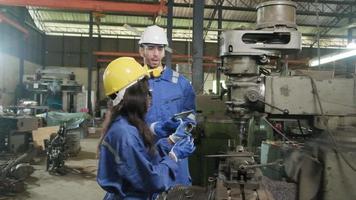 dos trabajadores industriales con uniformes de protección y seguridad y cascos, un gerente masculino y un colega negro trabajan con máquinas de metalurgia en la fábrica de fabricación. equipo profesional de ingenieros de producción. video