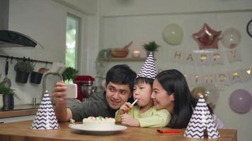 el padre y la madre están organizando una fiesta de cumpleaños para su hijo que tiene 5 años. el padre y la madre toman una foto y un video en vivo para la abuela y el abuelo a distancia social.