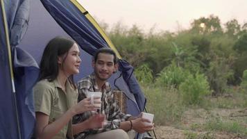 una pareja está teniendo una velada el día de vacaciones. los hombres y las novias disfrutan de la bebida y la naturaleza mientras acampan. viajes de recreación y concepto de camping. video