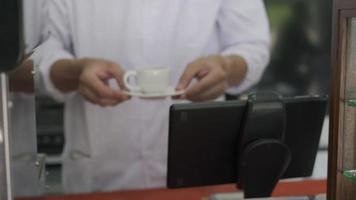 le barista faisait du café selon la recette et tenait la tasse de café devant le client. le propriétaire d'un petit café prépare du café avec des grains de café arabica pour servir aux clients. video