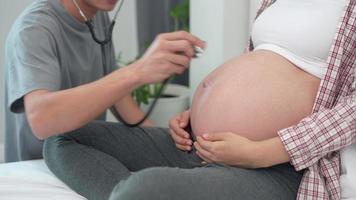 concetto incinta donne e marito. marito è utilizzando un' stetoscopio per sentire per ascoltando cuore di bambino voce. ascoltando per il suono di il nascituro bambino rilevamento possibile anomalie. video