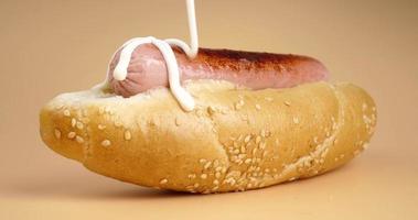 pour mayonnaise sauce on a hot dog closeup, bun and sausage fast food video