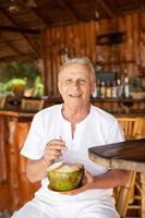 un anciano feliz está bebiendo agua de coco en el bar de la playa foto