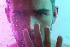 Portrait of handsome man through wet glass in neon light photo