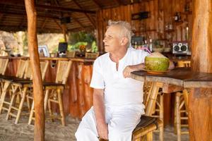 un anciano feliz está bebiendo agua de coco en el bar de la playa foto