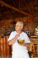 Happy senior man is drinking a coconut water in the beach bar photo