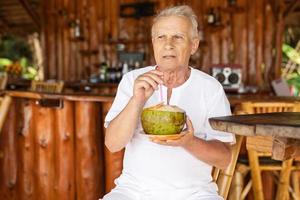 un anciano feliz está bebiendo agua de coco en el bar de la playa foto