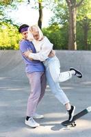 Carefree teenager couple in a skate-park. Guy giving a lesson of skateboarding for his girlfriend. photo