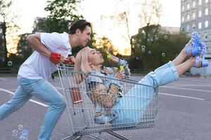 una pareja joven se divierte con un carrito de compras en el estacionamiento de un supermercado foto