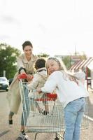 Happy mother and her daughters are having fun with a shopping cart on a parking lot beside a supermarket. photo