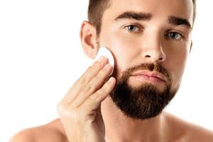 Young handsome man is cleaning his face with a cotton pad photo