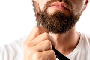 Man is shaving his thick beard with a straight razor photo