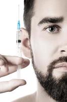 Handsome man holding syringe with a filler on white background photo