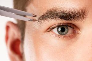 Male eye and tweezers for eyebrow grooming and shape correction photo