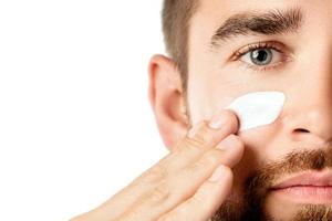 Young man is applying moisturizing and anti aging cream on his face photo