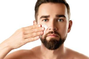 Young man is applying moisturizing and anti aging cream on his face photo