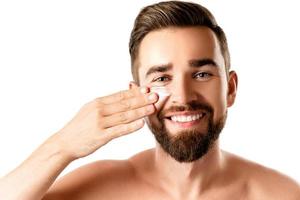 Young man is applying moisturizing and anti aging cream on his face photo