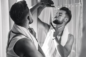 Man looking in the mirror, smoking a cigarette and shaving his beard with a straight razor photo