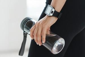 emale hand with smartwatch holding reusable bottle with water. photo