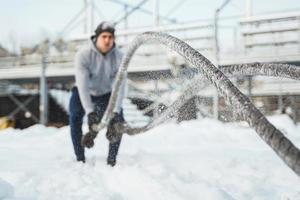 Young athlete working out with a battle ropes during snowy winter day. photo