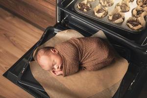Newborn baby is lying on the oven tray with a muffins photo