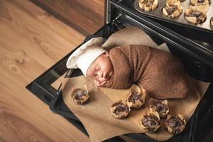 un bebé recién nacido con sombrero de chef está tirado en la bandeja del horno con muffins foto