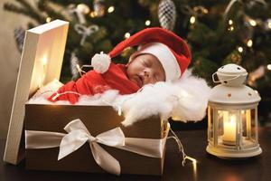 lindo bebé recién nacido con sombrero de santa claus está durmiendo en la caja de regalo de navidad foto