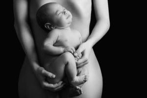 Little newborn baby lying on the mother belly on black background photo