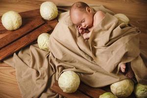 Little baby is lying in the box with a lot of cabbages around photo