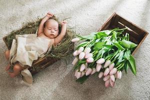 Cute little baby is lying in the wooden box and heap of pink tulips photo