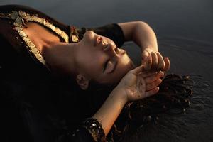 Sexy woman wearing black tunic is posing on the beach with black sand photo