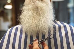 peluquero cortando la barba de un anciano con unas tijeras foto