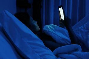 mujer joven está usando un teléfono inteligente en la noche en la cama foto