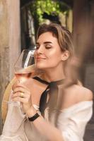 mujer joven está bebiendo vino rosado en el bar de la calle