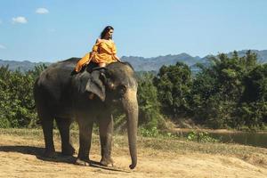 Woman wearing beautiful orange dress is riding the elephant photo