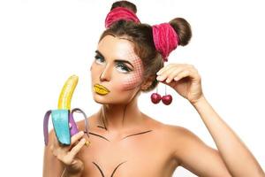 Beautiful model with creative pop art makeup holding banana and cherries photo