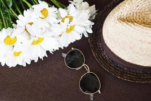 Stylish straw hat, sunglasses and chamomile flowers. photo